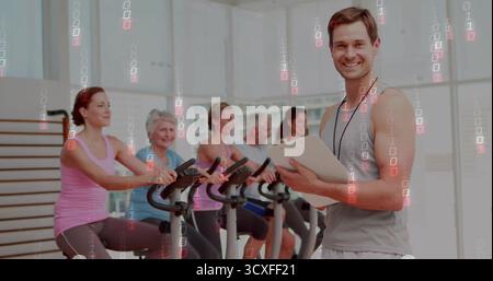 Leading male fitness instructor with clipboard guiding class on stationary bikes in gym, copy space Stock Photo