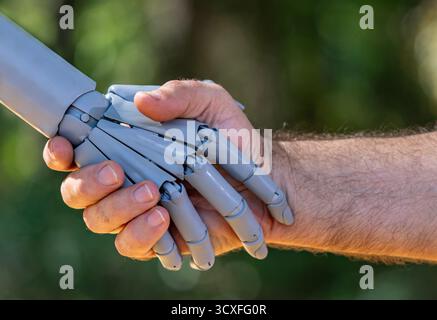 Robot and human hands. Robot and male hand handshake on green nature. Ai and human hands making handshake. Robotic hands interacting with human hand Stock Photo