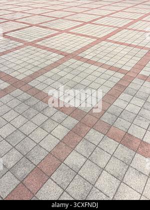 Pavement surface showing a repeating geometric pattern of square tiles and intersecting red lines Stock Photo