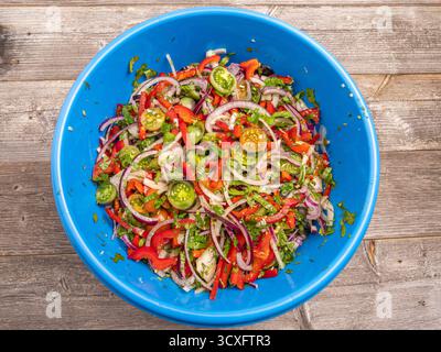 Fresh vegetable salad with cherry tomatoes, onions, peppers, and herbs in a blue bowl, top view. Stock Photo