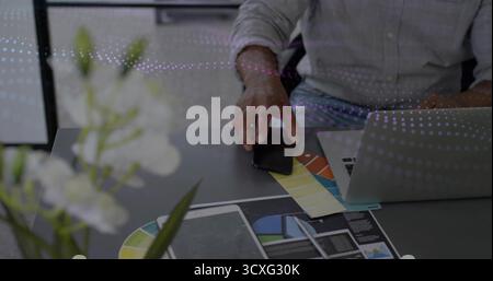 Designer in shirt with rolled sleeves selecting color from swatch at office desk, laptop layouts Stock Photo