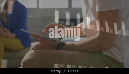 Man wearing smartwatch reviewing data with stylus on tablet in office lounge, projecting bar chart Stock Photo