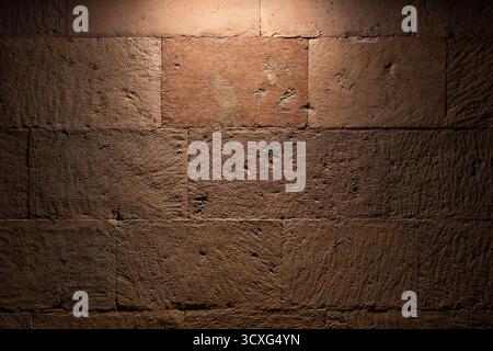 A close-up view of a rough brown stone wall illuminated from above, revealing gritty textures and warm tones. Great for architectural, interior, or ba Stock Photo