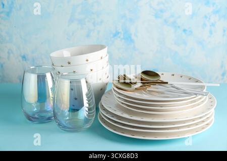 Clean glass cups with bowls, plates and cutlery on blue table against grunge wall Stock Photo