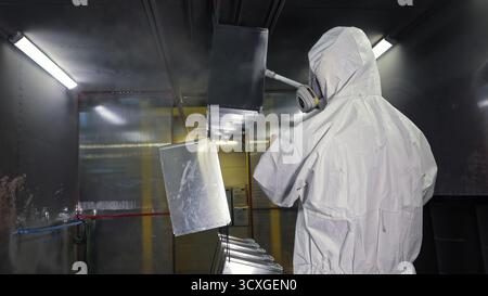 Worker in protective suit spray-painting metal parts. Industrial worker in hazmat suit using a spray gun to paint metal components inside a controlled Stock Photo