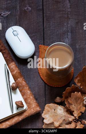 Business concept. A cozy autumn still life with office supplies, a computer mouse, pen, notebook, coffee, and a scarf. Rustic style. Stock Photo
