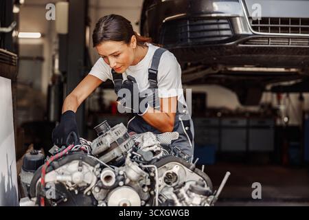 A skilled female mechanic is diligently working on an engine within her garage workshop Stock Photo