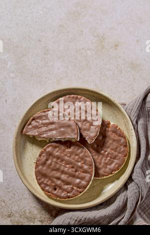 plate of rice galettes cakes cookies covered with milk chocolate and glass of milk on beige background, top view Stock Photo