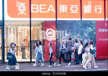 Pedestrians walk past the Bank of East Asia (BEA) branch and logo in Hong Kong. Stock Photo