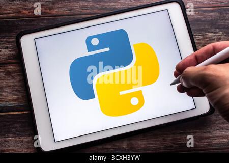 Quito, ECUADOR - Oct 14 2025 : Logo of Python on tablet on wooden table. Man hand holding wireless stylus pen Stock Photo