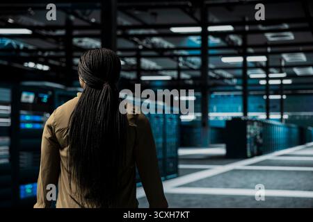 Software developer walking through server room rows lined with storage infrastructure rigs. IT worker inspecting high tech data center helping power internet services for business clients Stock Photo