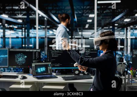 Data center technician monitoring AI systems using virtual reality, adjusting deep learning parameters. Server room IT expert wearing VR headset enhancing neural networks performance Stock Photo