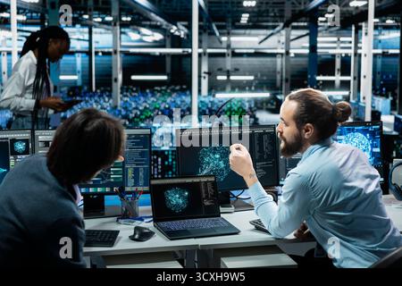 Team of programmers in data center installing upgraded server racks systems helped by AI technology. Server room coworkers talking, upgrading enterprise networks hardware using artificial intelligence Stock Photo