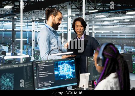 Programmers working together, coding in data center, updating deep learning scripts. Asian man and coworker in server hub programming artificial intelligence algorithms, debugging equipment racks Stock Photo