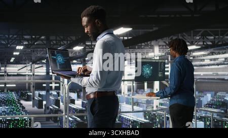 Server hub teamworking IT experts visualizing large language model architecture using notebook. Data center system administrators on industrial platform collaborating on tasks using laptop Stock Photo