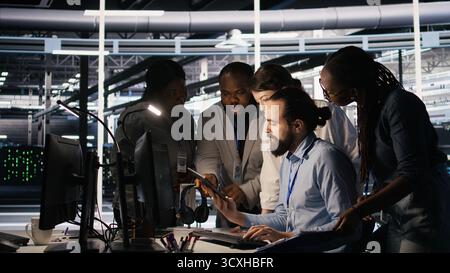 Admins doing brainstorming in server hub, reviewing machine learning code and LLM visualization dashboards. Data center IT experts using computer to monitor AI infrastructure performance, camera A Stock Photo