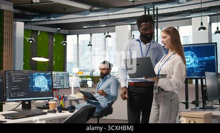 Junior dev and colleague in office reviewing AI system metrics, monitoring performance dashboards. Tech company programmer and young female engineer tuning neural networks, camera A Stock Photo