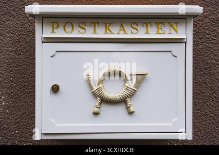 White mailbox with historic post horn relief hanging on a brown wall outside Stock Photo