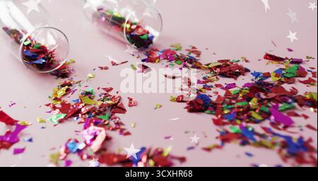 Colorful confetti scattered from glass over star image on pink background Stock Photo