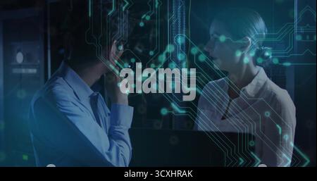 Discussing IT professionals analyzing data flow in server room with open laptop, circuitry overlay Stock Photo