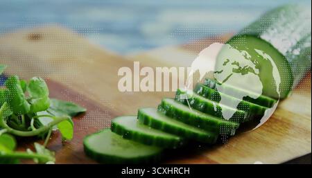 Displaying halved cucumber with sliced rounds on kitchen prep board, floating globe map with greens Stock Photo