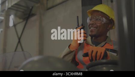 Operating forklift operator wearing safety gear holding walkie-talkie inside warehouse, copy space Stock Photo