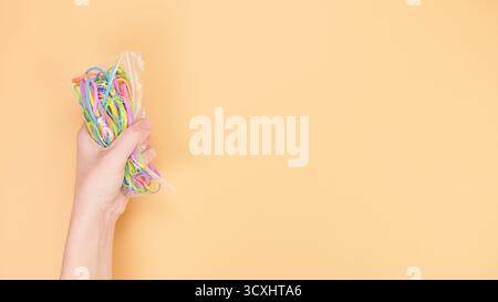 A hand holds a plastic bag filled with vibrant rubber bands against a bright orange background. This fun image suits themes of crafting, fashion, or s Stock Photo
