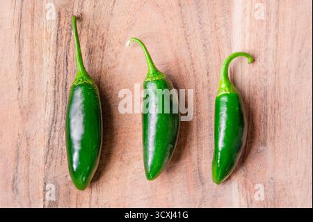 Three whole jalapeno peppers lined up on a wood cutting board Stock Photo