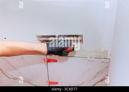Construction worker uses trowel to spread tile adhesive on wall during bathroom remodel Stock Photo