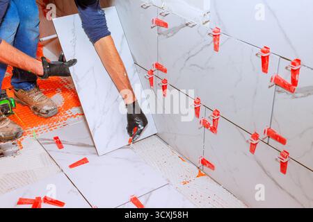 Expert tiler laying large marble tiles on bathroom wall using spacers to ensure even gaps. Stock Photo
