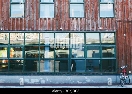 HAKODATE, JAPAN: A symmetrical, graphic facade of a rustic red wooden warehouse with large windows reflecting the sky in the historic bay area. Stock Photo