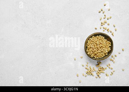 A wooden bowl filled with golden pine nuts on a light gray textured surface. Some nuts are scattered around the bowl, creating a natural and organic f Stock Photo