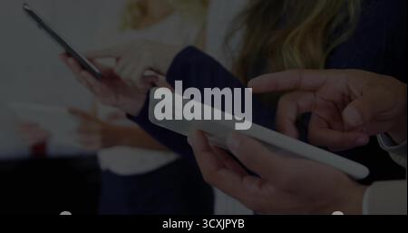 Standing four professionals in business attire holding smartphones and tablets in meeting room Stock Photo