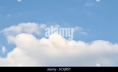 A serene sky background featuring a large, fluffy cumulus cloud that dominates the bottom frame, set against a soft and clear pale blue sky above, per Stock Photo