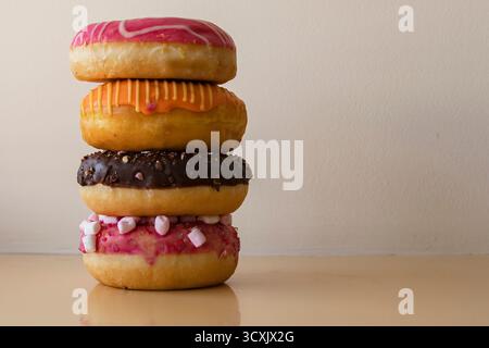 Stack of colorful donuts with pink orange and chocolate glaze on beige background Stock Photo
