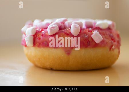 Pink glazed donut with marshmallows and sugar sprinkles on wooden table Stock Photo