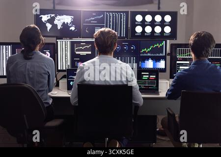 Stock traders working on multiple computer screens showing charts and graphs Stock Photo
