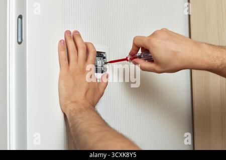 electrician working on light switch using screwdriver inside, close-up Stock Photo