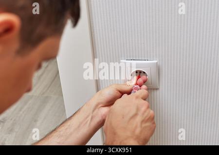 electrician installing electrical socket in white plastic frame with a screwdriver at home Stock Photo