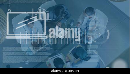Collaborating team leaning over charts around glass table in office, with laptops and stethoscopes Stock Photo