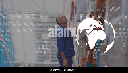 Worker in navy uniform checking boxes on shelves in warehouse aisle, with world map overlay Stock Photo