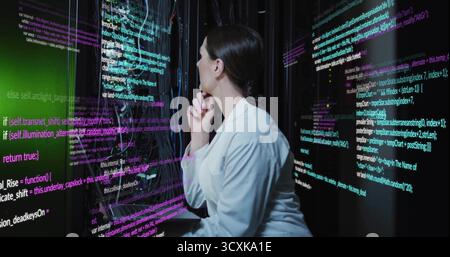 Analyzing female specialist reviewing code in data center with display panels, server racks, cables Stock Photo
