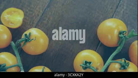 Displaying yellow cherry tomatoes on wooden kitchen tabletop, with green vines, halved tomato Stock Photo