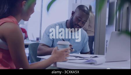 Writing adult Black man wearing blue polo shirt completing documents in office, with silver laptop Stock Photo