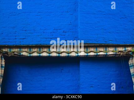 Striped fabric awning against a bright blue painted brick wall. Stock Photo