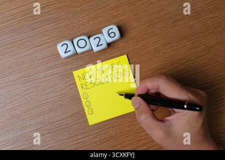 Top view image of yellow paper with the words "NEW YEAR'S RESOLUTIONS" written on it and cube with 2026 number. New Year Resolutions concept. Stock Photo