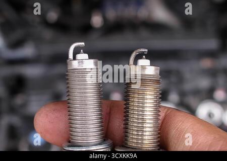 Mechanic hand holding new and used spark plugs side by side, close up comparison of car ignition parts, automotive maintenance and engine performance Stock Photo