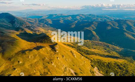 Aerial view of sunlit mountain ridge and distant forested valleys under clear sky Stock Photo