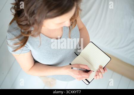 Top-down view of pregnant female writing important delivery notes in journal. Thoughtful preparation for maternity hospital stay and baby arrival. Stock Photo