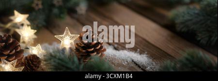 Panoramic Christmas background with dark wood, pine cones, fir branches and star shaped lights Stock Photo